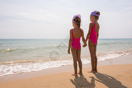两个穿泳衣的女孩站在沙滩上看海图片