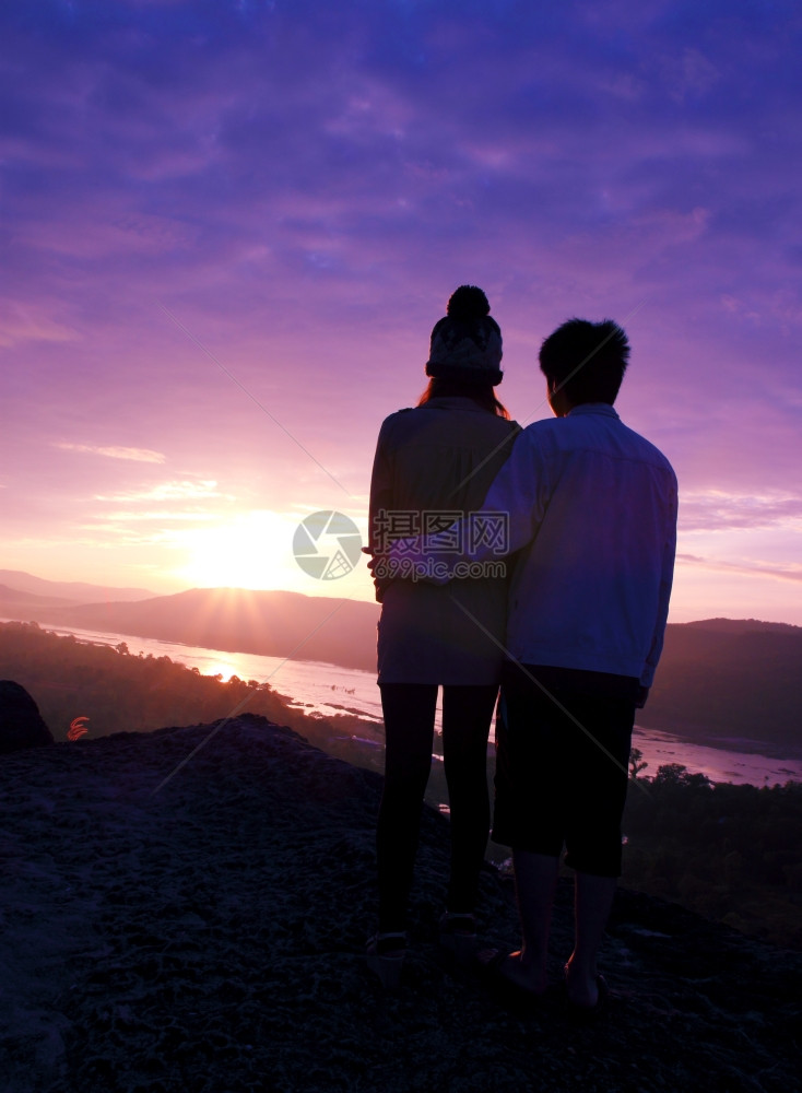 一对夫妇在日出时站悬崖上图片