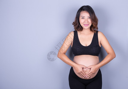 孕妇将手握在腹部的心脏形状中图片