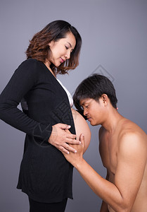 年轻男人用灰墙背景亲吻怀孕妻子的肚背景图片