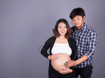 男用听诊器在灰墙上怀孕妻子的腹部图片