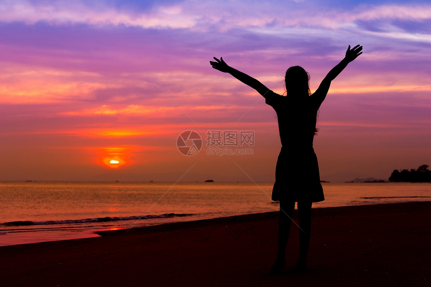 日落时站在海边的沙滩上手举起女人的休眠图片