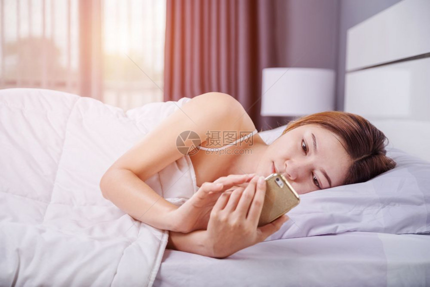 女人用她的智能手机在卧室的床上用柔软灯光图片