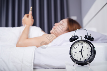 手机时钟素材女人在卧室的床上用智能手机背景