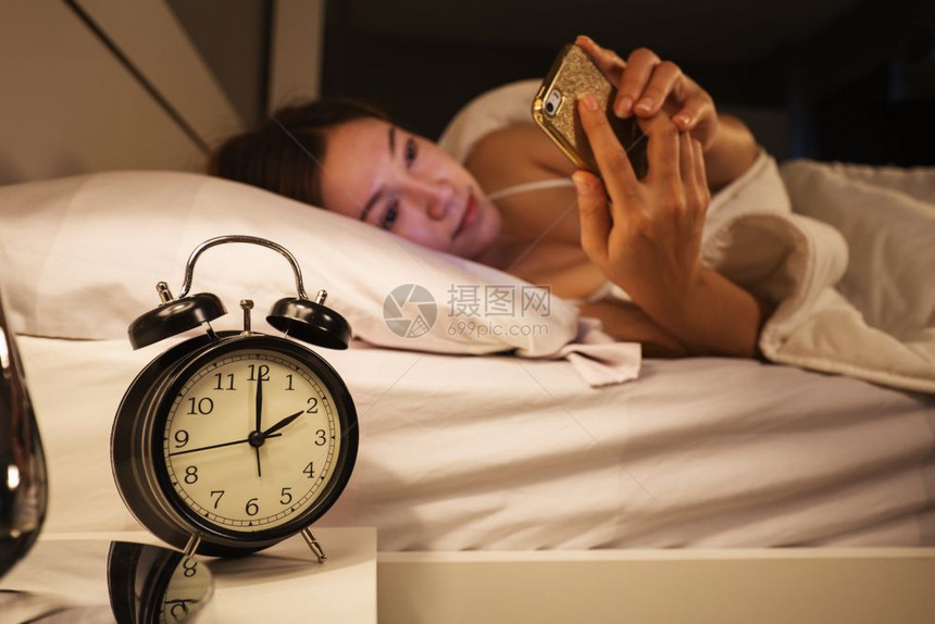 时钟显示2点和女人使用智能手机在卧室的床上图片