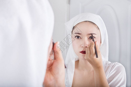美丽的女人看着镜子用铅笔化妆眉毛图片