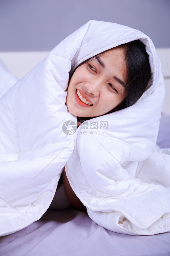 幸福的女士躲在毯子下躺卧室的床上图片