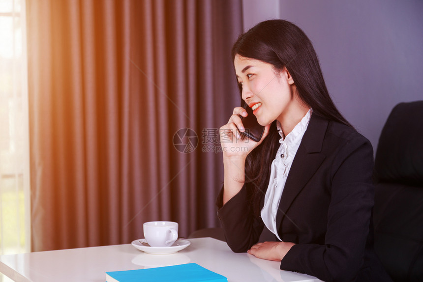 坐在办公桌边手机上聊天的年轻女商人图片