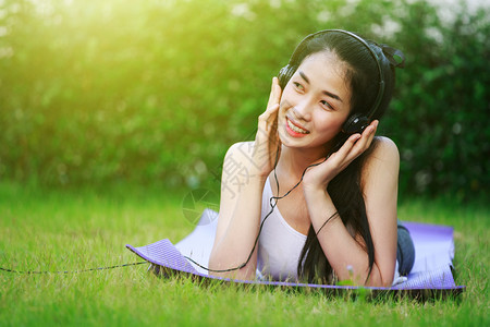 年轻妇女用耳机听音乐躺在草地上图片