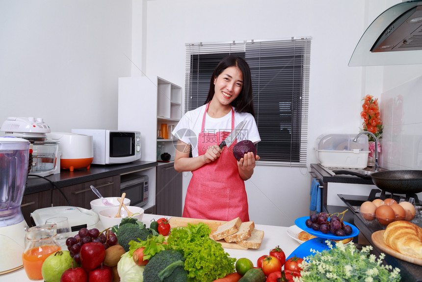 在家里的厨房拿着紫色卷心菜和刀子的快乐女人图片