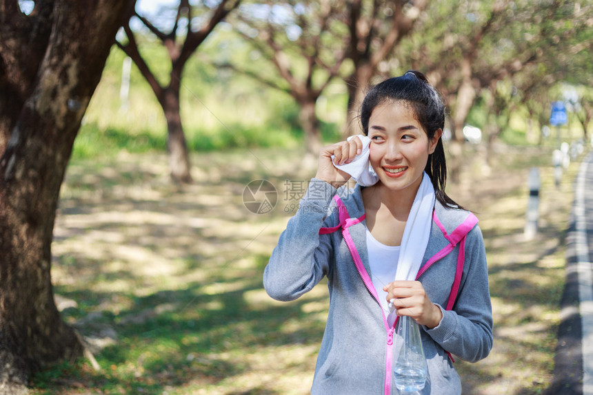 在公园户外运动锻炼后年轻女在公园休息用毛巾擦汗图片