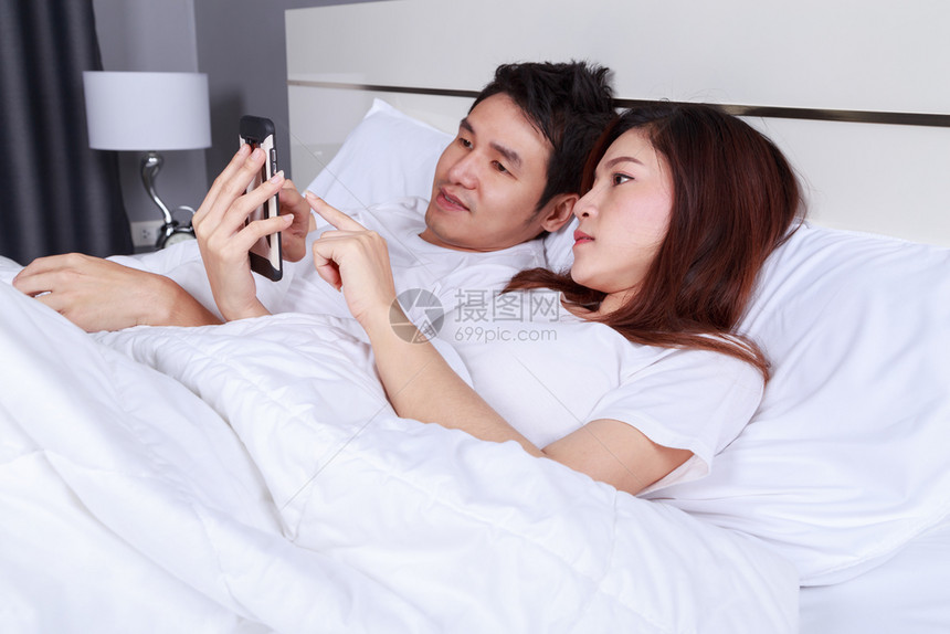 在卧室的床上使用手机年轻夫妇图片