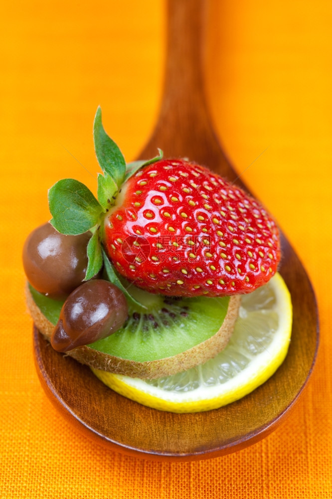 柳草莓椰菜和巧克力糖放在橙色布料的木勺子里图片