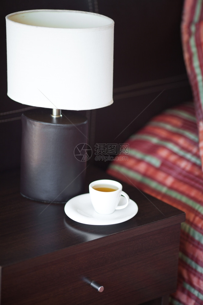 床铺有枕头边桌子和灯台上有杯茶图片