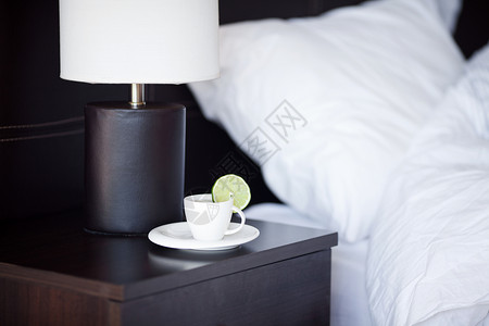 床铺有枕头边桌子和灯台上有杯茶背景图片