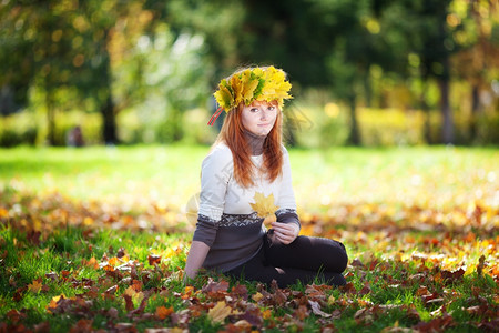 年轻的红发少女戴着枫叶花环坐在草地上图片