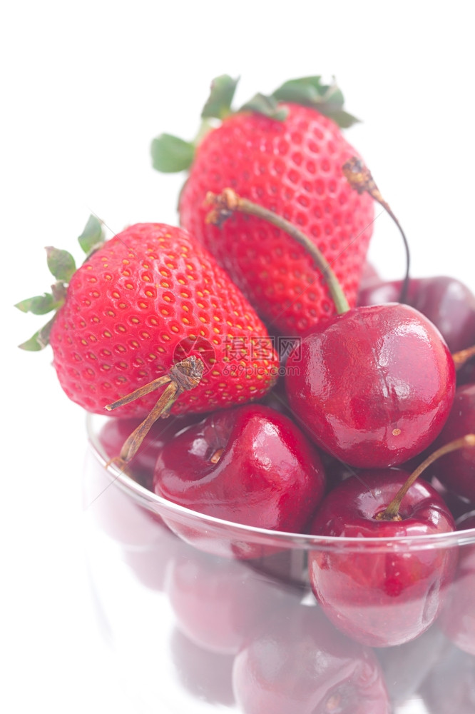 在一个玻璃碗中的樱桃和草莓孤立在白色上图片