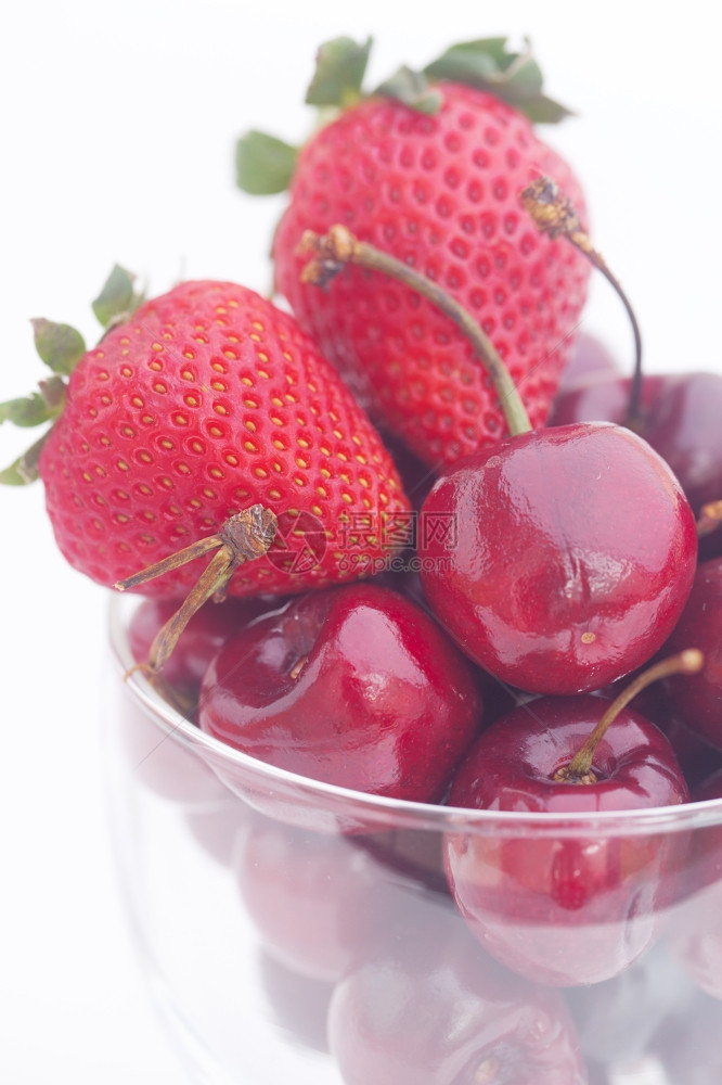 在一个玻璃碗中的樱桃和草莓孤立在白色上图片