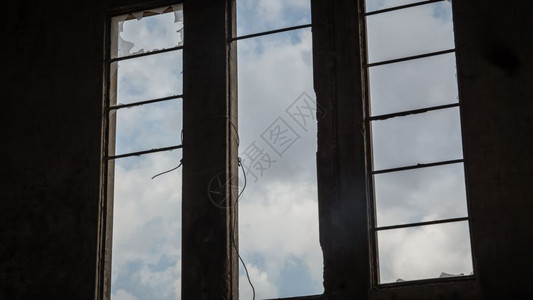 一个废弃建筑的破碎窗口从内部查看天空窗外看到云层图片