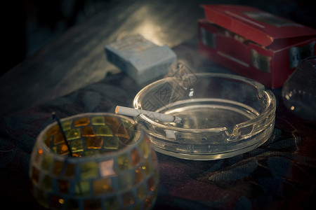 在玻璃烟灰缸里点燃香烟烟灰缸放在桌布上戏剧紧张气氛图片