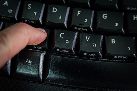 男人在无线键盘上打字用希伯来语和英字母打按剪切钮顶视图黑暗气氛图片