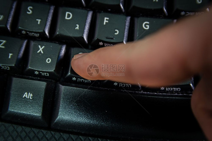 用希伯来语和英字母在无线键盘上打字的人按复制钮顶视图黑暗气氛图片