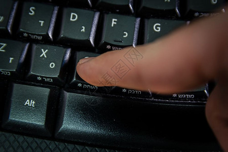 用希伯来语和英字母在无线键盘上打字的人按复制钮顶视图黑暗气氛图片