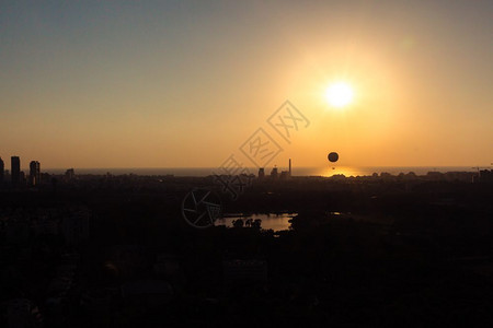 日落时特拉维夫天际线日落时光环可以看到一个热气球在空中飞翔此外还可以看到北特拉维夫哈亚肯公园阅读电站和地中海的附近区背景