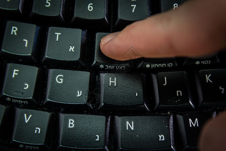 男人在无线键盘上打字用希伯来语和英字母打按Redo钮顶视图黑暗气氛图片