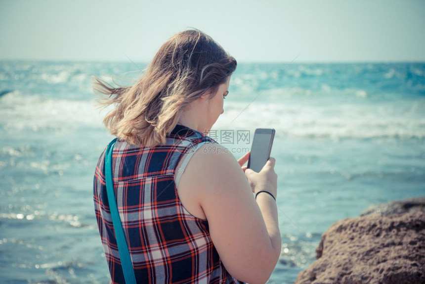 女人在海边的滩上使用她的智能手机户外图片