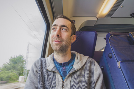 年轻人在火车上旅行望着窗外微笑一个蓝色的手提箱在他旁边图片
