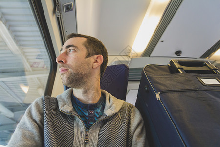 年轻人坐在火车上看着窗外旁边有个蓝色的手提箱图片