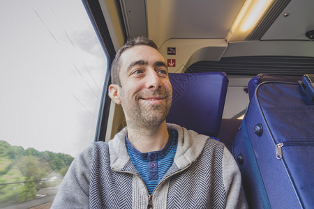 年轻人在火车上旅行对着别人微笑蓝色的手提箱在他旁边图片