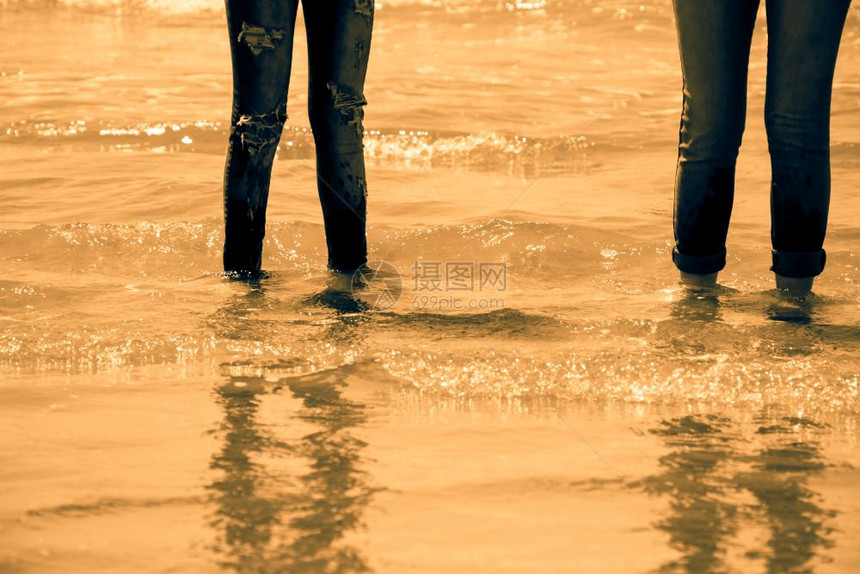 身穿蓝色牛仔裤的女子站在海岸的水里金色音调图片