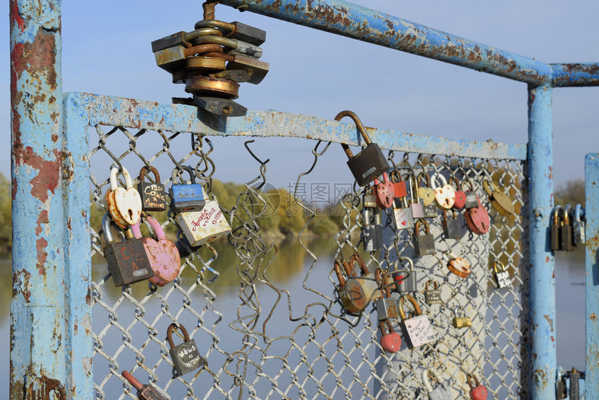 新婚夫妇和恋人挂在河边的栅栏上爱锁是牢固关系和永恒爱的象征俄罗斯克拉诺达尔2017年月4日新婚夫妇和恋人挂在河边的栅栏上爱锁牢固图片