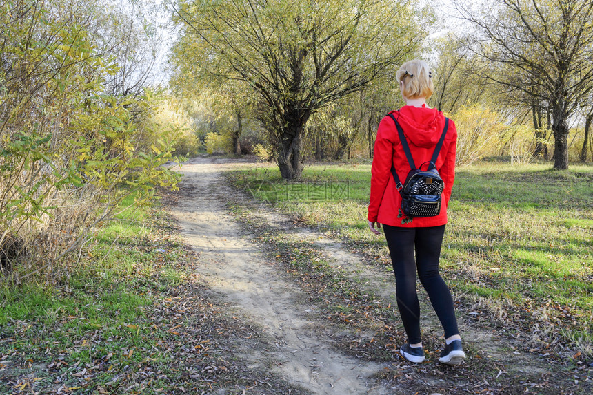 女孩穿着红色夹克背包走在通往森林的路上起点女孩穿着红色夹克背包走在通往森林的路上图片