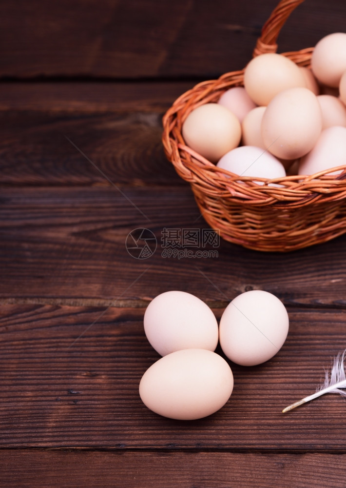 褐木表面的新鲜鸡蛋后面的一篮子鸡蛋图片