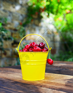 棕色桌子上黄色铁桶里的红色成熟樱桃黄铁桶里的红熟樱桃图片