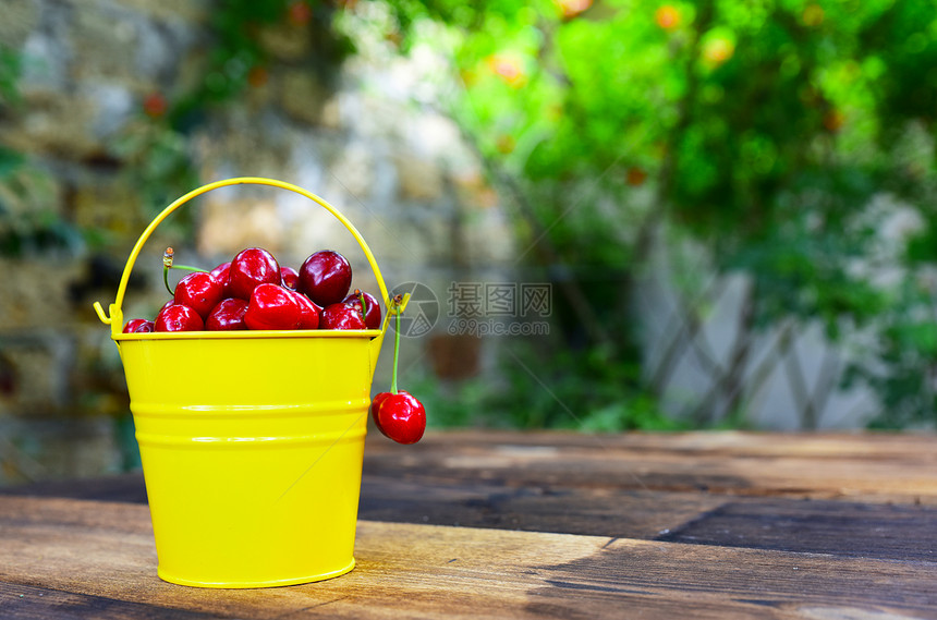 红樱桃在棕色木制桌子上的黄色桶背景模糊红樱桃在棕色木制桌子上的黄色桶图片