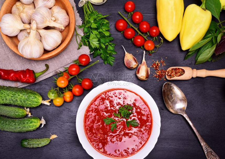 新鲜的冷番茄和蔬菜汤加松在白圆盘中黑底的铁勺子围绕原料和香图片