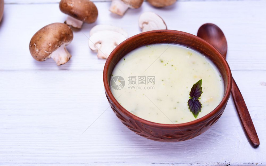 薄蘑菇奶油汤放在粘土棕色板块中白桌上有木勺子左边空图片