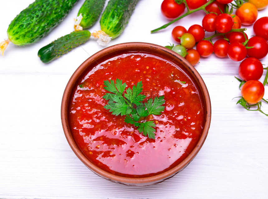 新鲜番茄和蔬菜的冷汤加萨帕乔放在白木桌的棕色圆板上图片