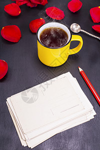 黑色背景上有红铅笔的空纸明信片旁边是黄杯茶叶顶视图图片