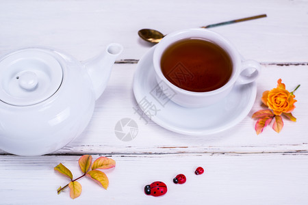 红茶装在一个白色的圆形杯子里茶托放在白色的木制背景上茶壶是白色的图片