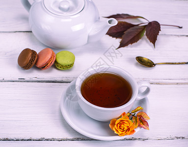 红茶在一个白色的圆形杯子里茶碟在白色的木制背景上蛋糕和麦卡龙图片