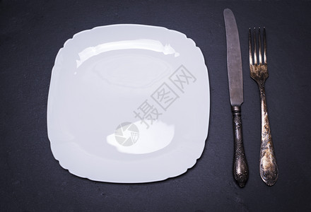 白色空方形瓷板和铁叉黑底顶视图上用刀刺铁叉背景图片