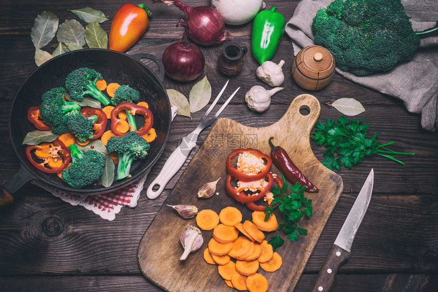 在木制厨房板上在圆面铁煎锅旁边的木制厨房板上有新鲜胡萝卜西兰花和红辣椒图片