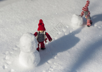 戴红帽子雪人两个玩具小男人白天在雪中玩耍背景