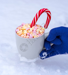 灰色杯子手拿着热巧克力和棉花糖与白雪相对图片