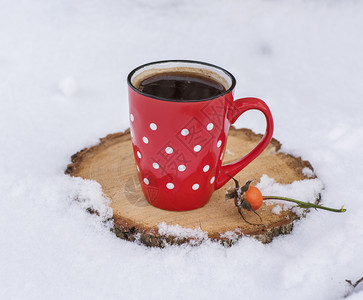 红陶瓷杯中的黑咖啡在雪中白波尔卡点在黄树上背景图片
